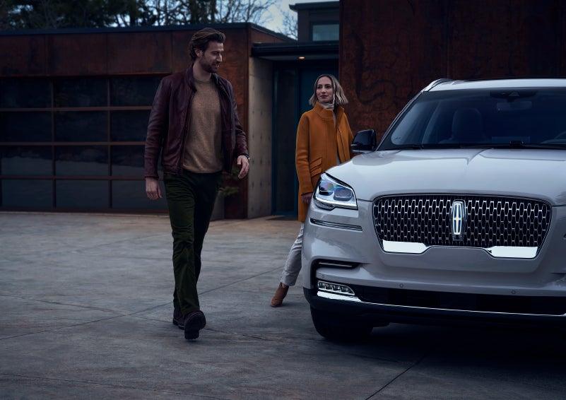 A man and a woman approaching a 2024 Lincoln Aviator® SUV, which illuminates certain lights when they are close | Lincoln Demo 4 in Derwood MD