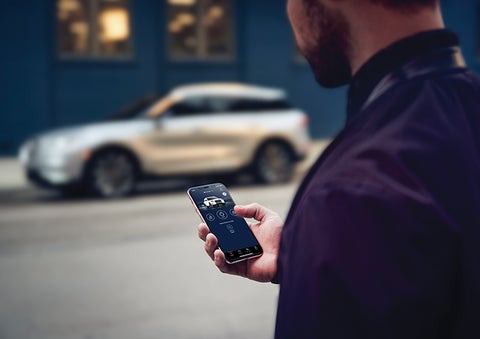 A person is shown interacting with a smartphone to connect to a Lincoln vehicle across the street. | Lincoln Demo 4 in Wooster OH