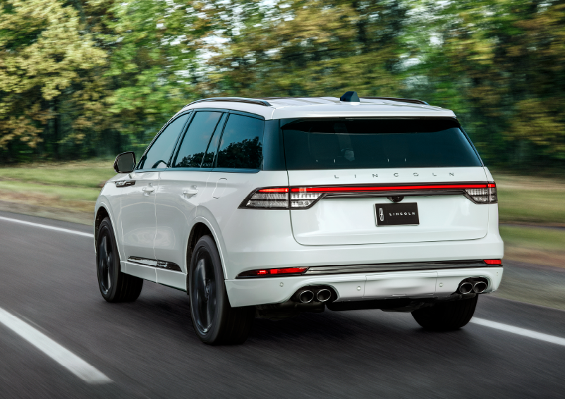 A white 2025 Lincoln Aviator® SUV is being driven away down a road lined with colorful trees. | Lincoln Demo 4 in Derwood MD