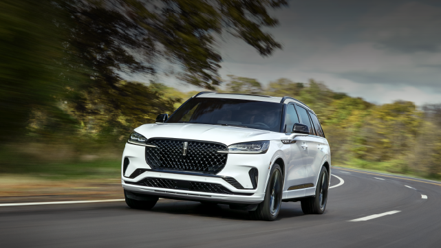 A white 2025 Lincoln Aviator® SUV is being driven down a road lined with trees. | Lincoln Demo 4 in Derwood MD